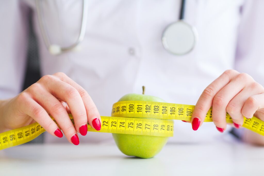 Doctor nutritionist measuring green apple in her office.